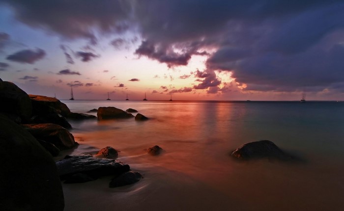 Sunset over the ocean with sailboats and rocks