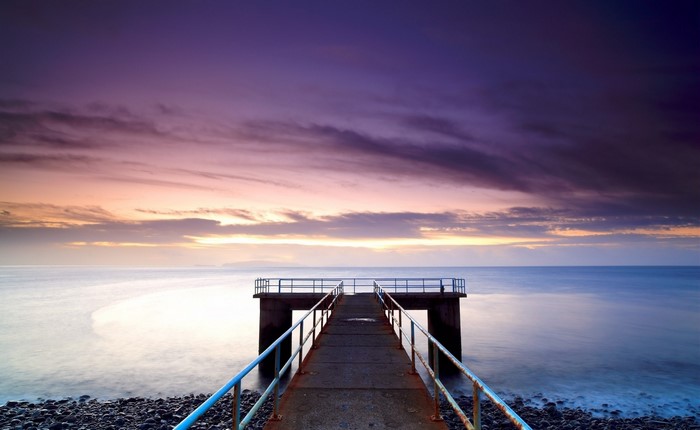 Pier extending into the ocean at sunset with purple clouds
