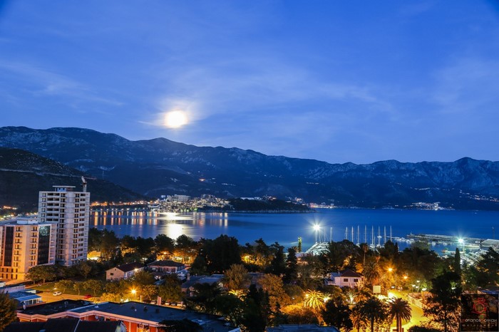 Cityscape at night with moon over mountains and bay
