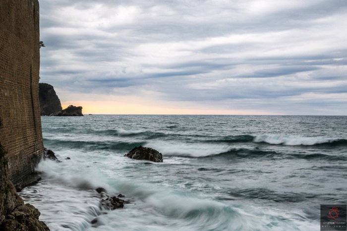 Long exposure of waves crashing against a brick wall and rocks by the sea