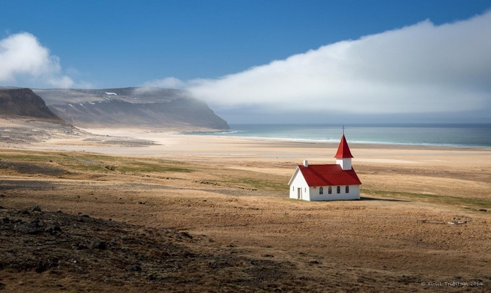 White chapel with red roof on a grassy shore by the sea