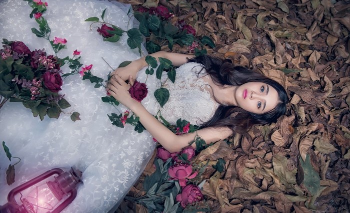 Woman in white dress lying among leaves and flowers with a lantern
