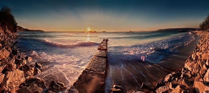 Sunset over the sea with a stone pier and rocky shore