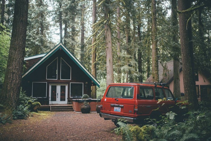 Red SUV parked by a cabin in a forest