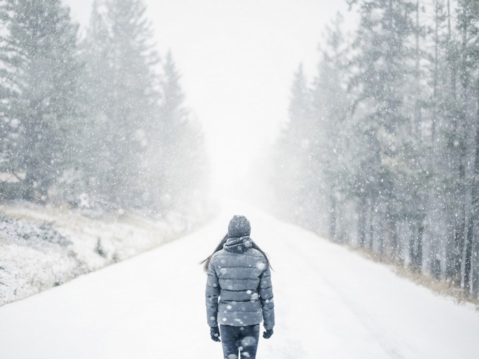 Woman walking on a snowy road surrounded by trees