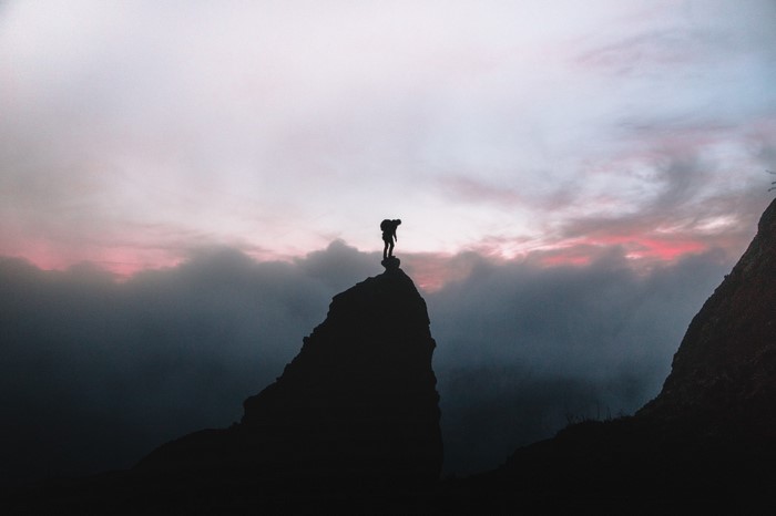 Silhouette of a hiker on a mountain peak at sunrise
