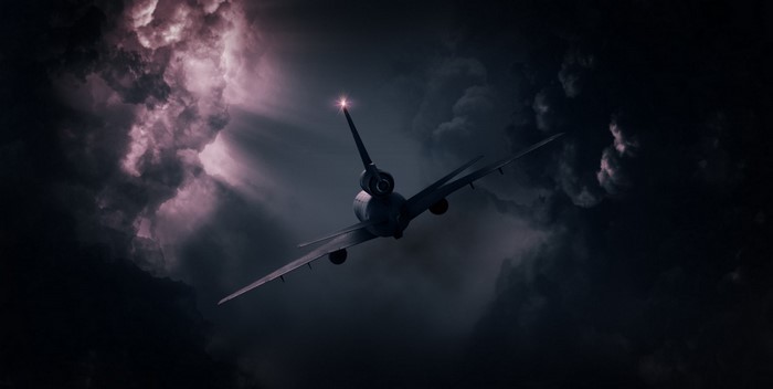 Airplane flying through dark stormy clouds with sun rays