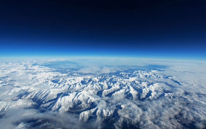 Aerial view of snow-covered mountains under a dark blue sky