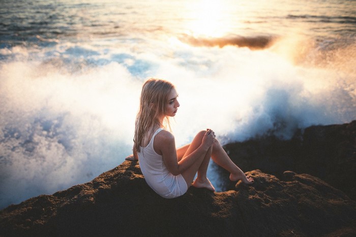Woman sitting on rocks by the sea at sunset