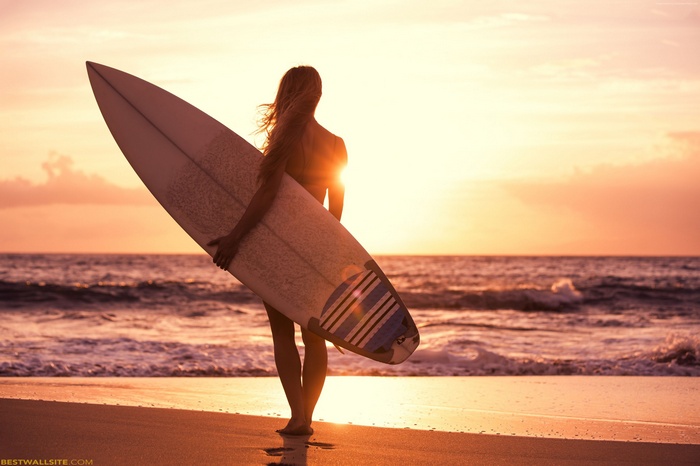 Girl with surfboard on beach at sunset