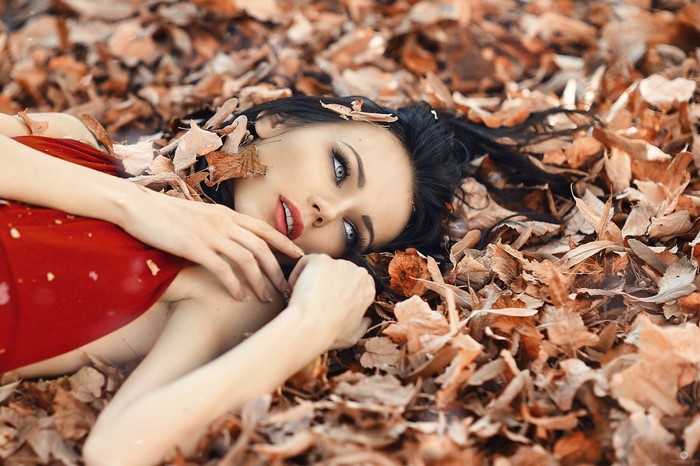 Woman in red dress lying in autumn leaves