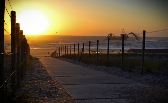Sunset over the sea with a ship and a beach path