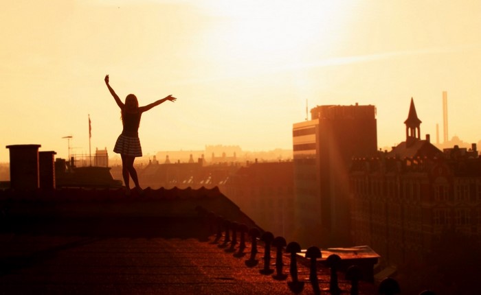 Silhouette of a woman with arms raised on a rooftop at sunset