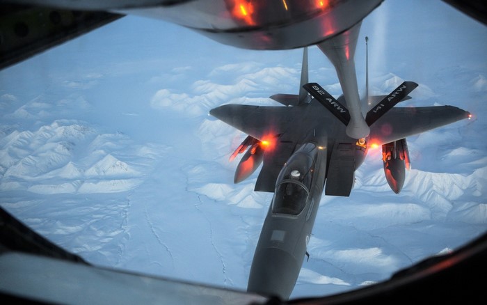 Mid-air refueling of F-15 Eagle fighter jet over snowy mountains