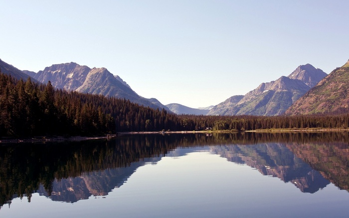 Mountain range reflected in a calm lake with pine forest