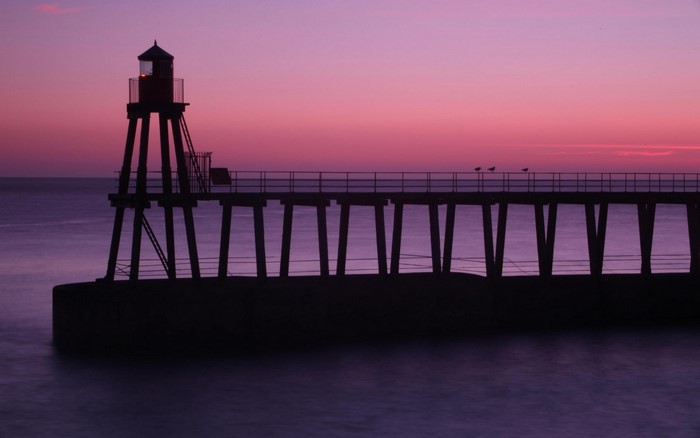 Silhouette of a lighthouse and pier at sunset over the sea