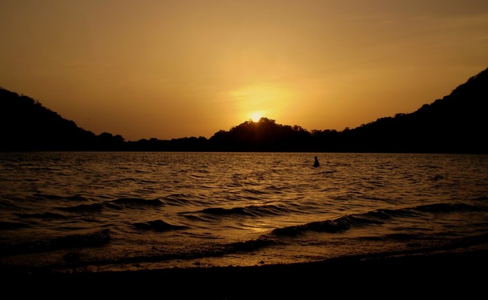 Sunset over a body of water with a person swimming