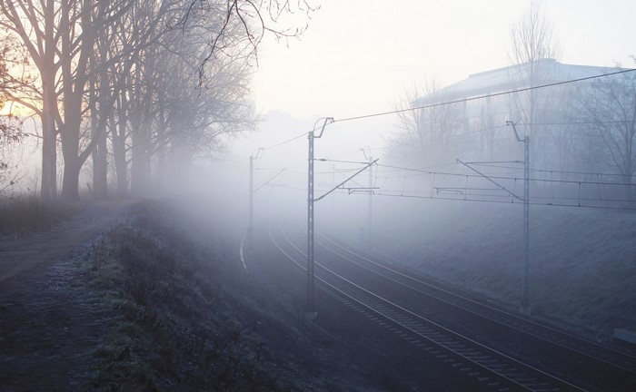Train tracks in the fog with trees and a building