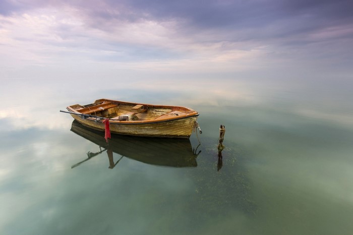 A lone wooden rowboat floats on calm water under a cloudy sky