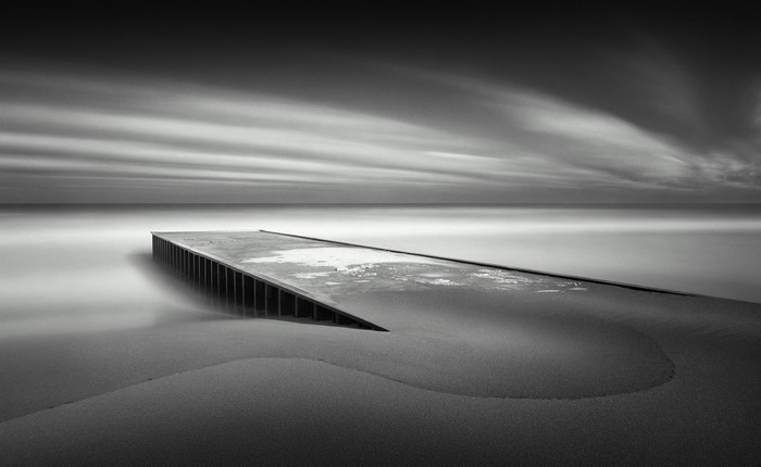 Monochrome pier on a sandy beach with blurred clouds over the sea