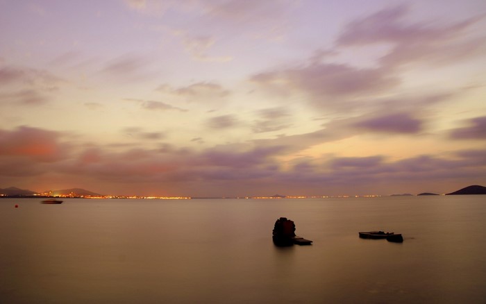 Sunset over a calm sea with distant city lights and rock formations