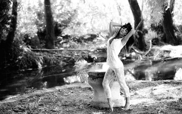 Woman in white lace posing by a stone in a forest