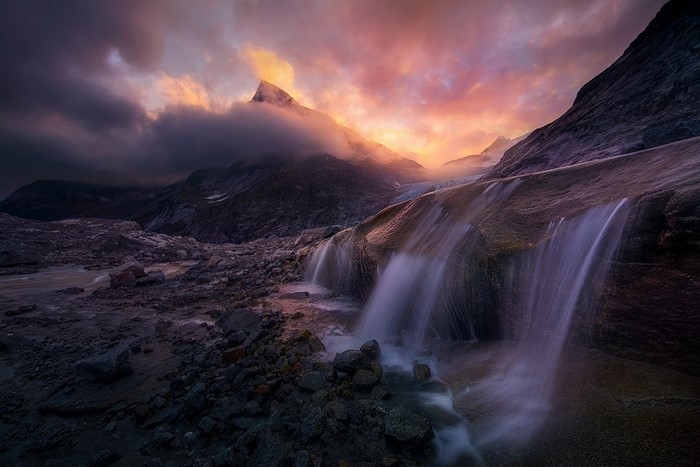 Waterfall flowing over rocks with mountain and sunset clouds