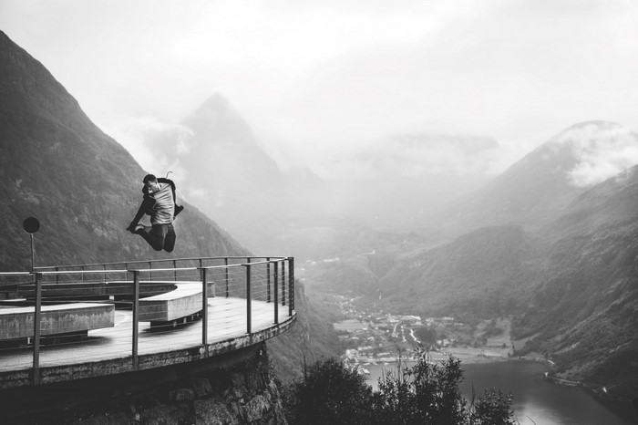 Man jumping on a viewpoint overlooking a fjord