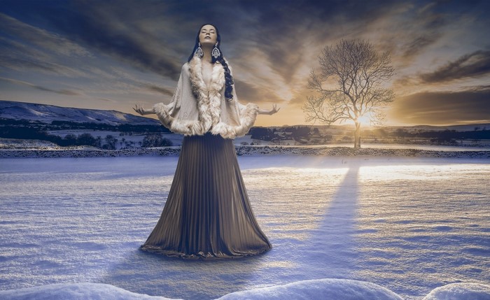 Woman in a fur-trimmed cape and dress in a snowy landscape at sunset