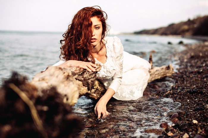 Woman in white dress lying on a log by the sea
