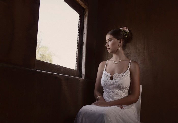 Bride in white dress looking out a window