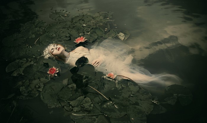 Woman in white dress floating among water lilies