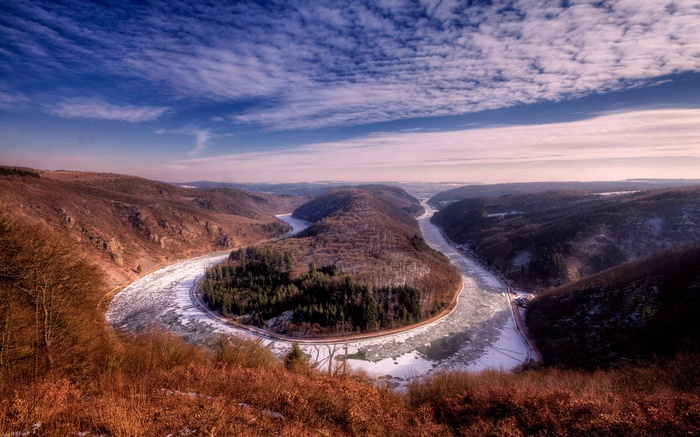 Frozen river bend in a forested valley under a cloudy sky