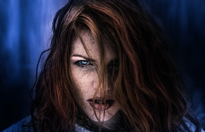 Woman with red hair and blue eyes in darkness