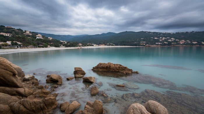 Long exposure of a rocky coast with a calm sea and distant hills