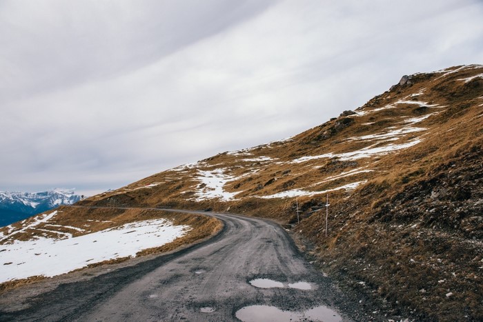 Winding mountain road with snow patches and distant mountains