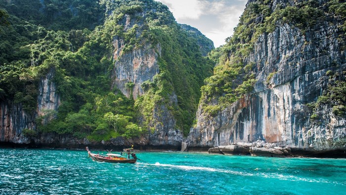 Boat sailing in a turquoise bay between cliffs in Thailand
