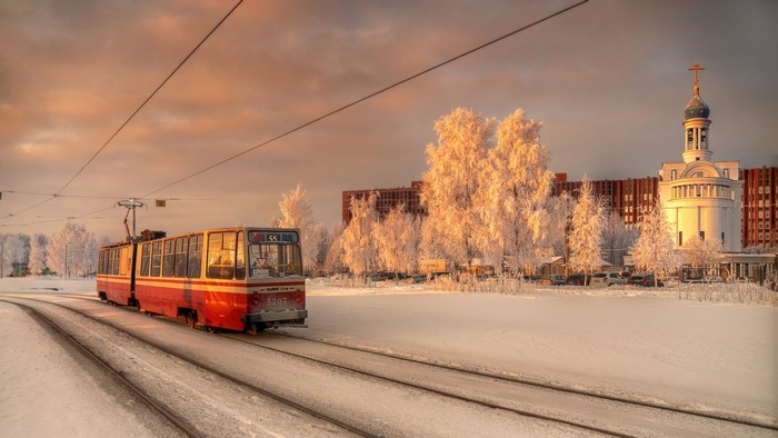 Red tram on snowy tracks in front of a church at sunrise