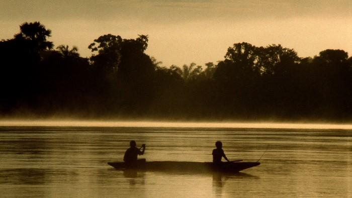 Two people in a canoe on a misty river at sunrise
