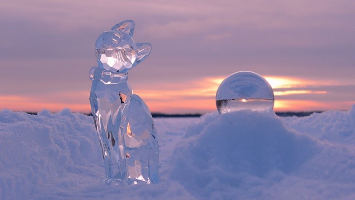 Ice cat sculpture and glass sphere in snow at sunset