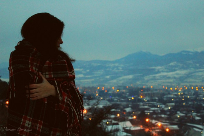 Woman wrapped in a blanket looking at a city at dusk