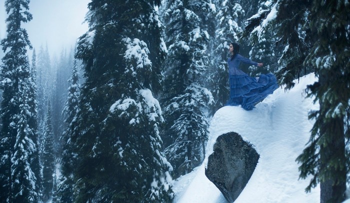 Woman in blue dress on snowy mountain cliff