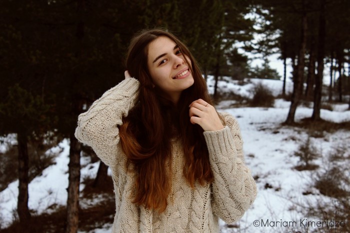Young woman in a knitted sweater in a snowy forest