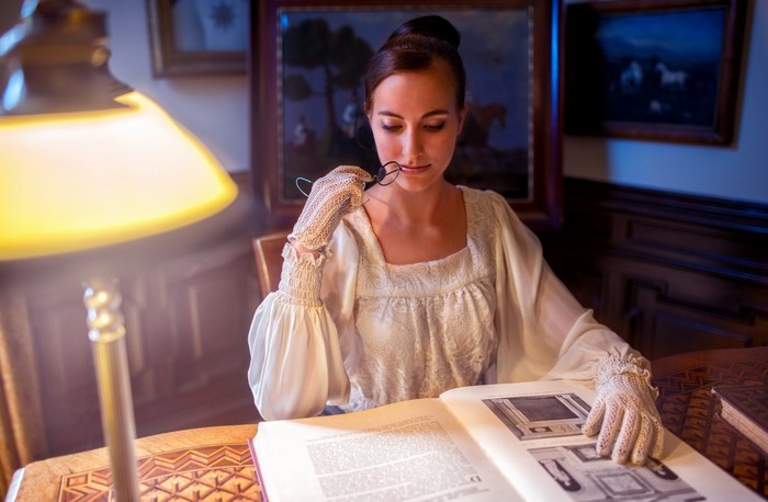 Woman in vintage dress reading a book by lamplight