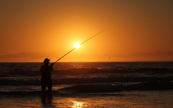 Fisherman casting a line at sunset over the ocean