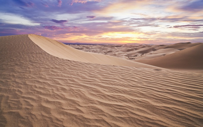 Desert sand dunes at sunset with colorful sky