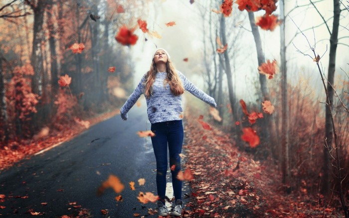 Woman in sweater and jeans in autumn forest with falling leaves