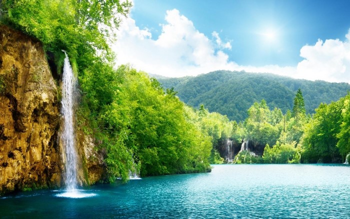 Waterfall cascading into a turquoise lake surrounded by green forest