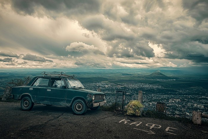 Old car parked on a cliff overlooking a city and mountains