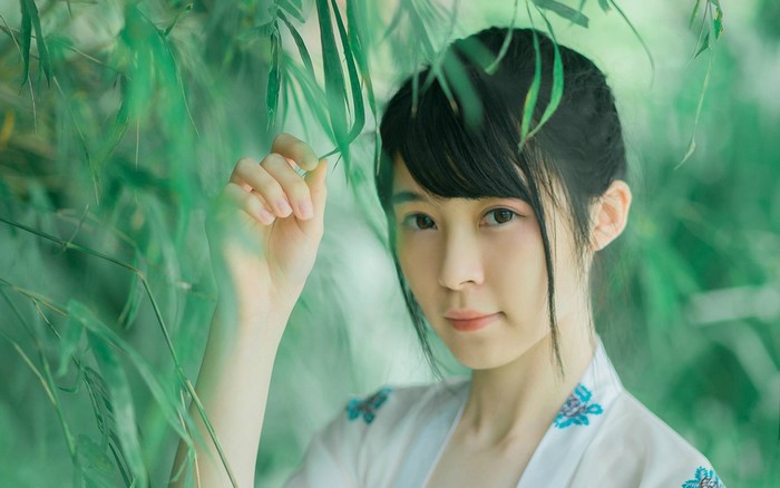 Young Asian woman in traditional dress among bamboo leaves